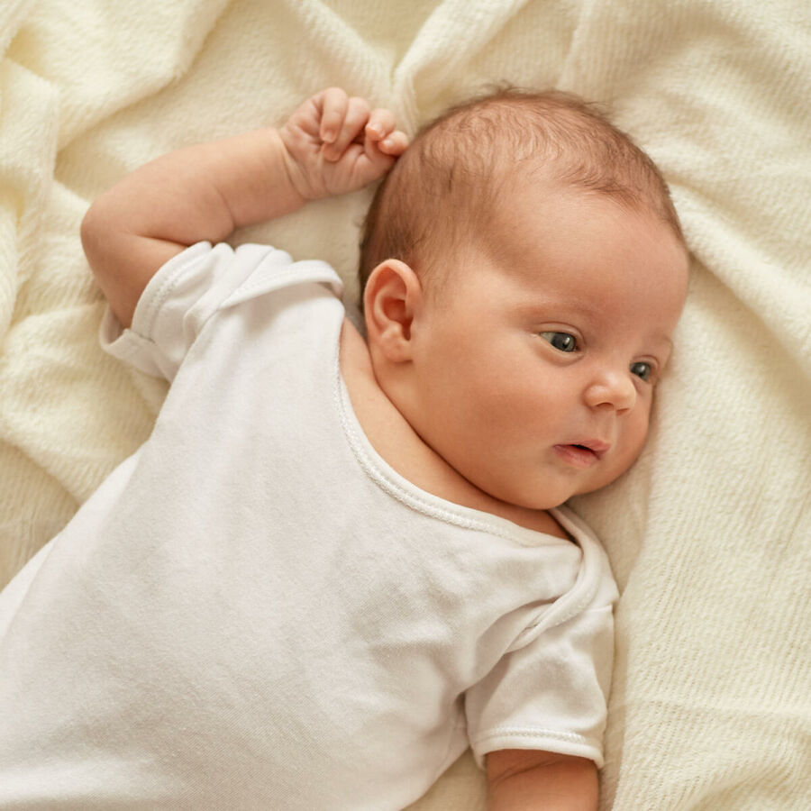 Imagem newborn-baby-girl-boy-lying-blanket-bed-looking-away-wearing-white-bodysuit-socks-infant-studying-world-around-has-sleepy-expression 1 1